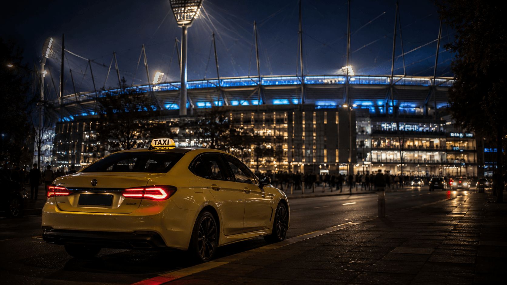Taxi waiting outside an illuminated Melbourne sports stadium at night after a major event