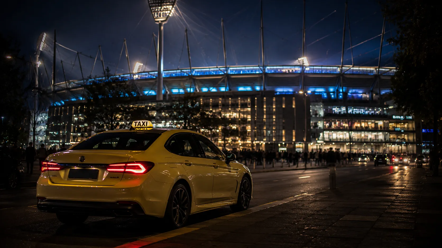 Taxi waiting outside an illuminated Melbourne sports stadium at night after a major event
